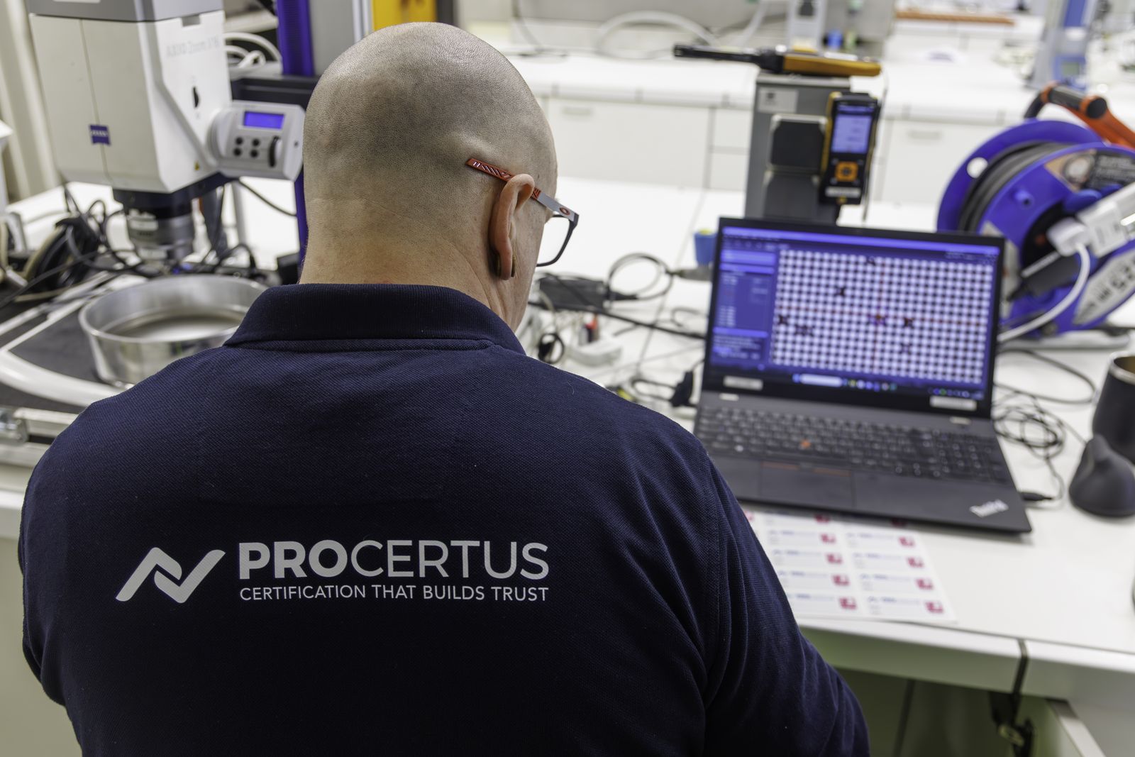 A Procertus engineer at a ZEISS microscope on-site, with the sieve mesh and its detected apertures displayed in the workflow on a laptop beside the instrument